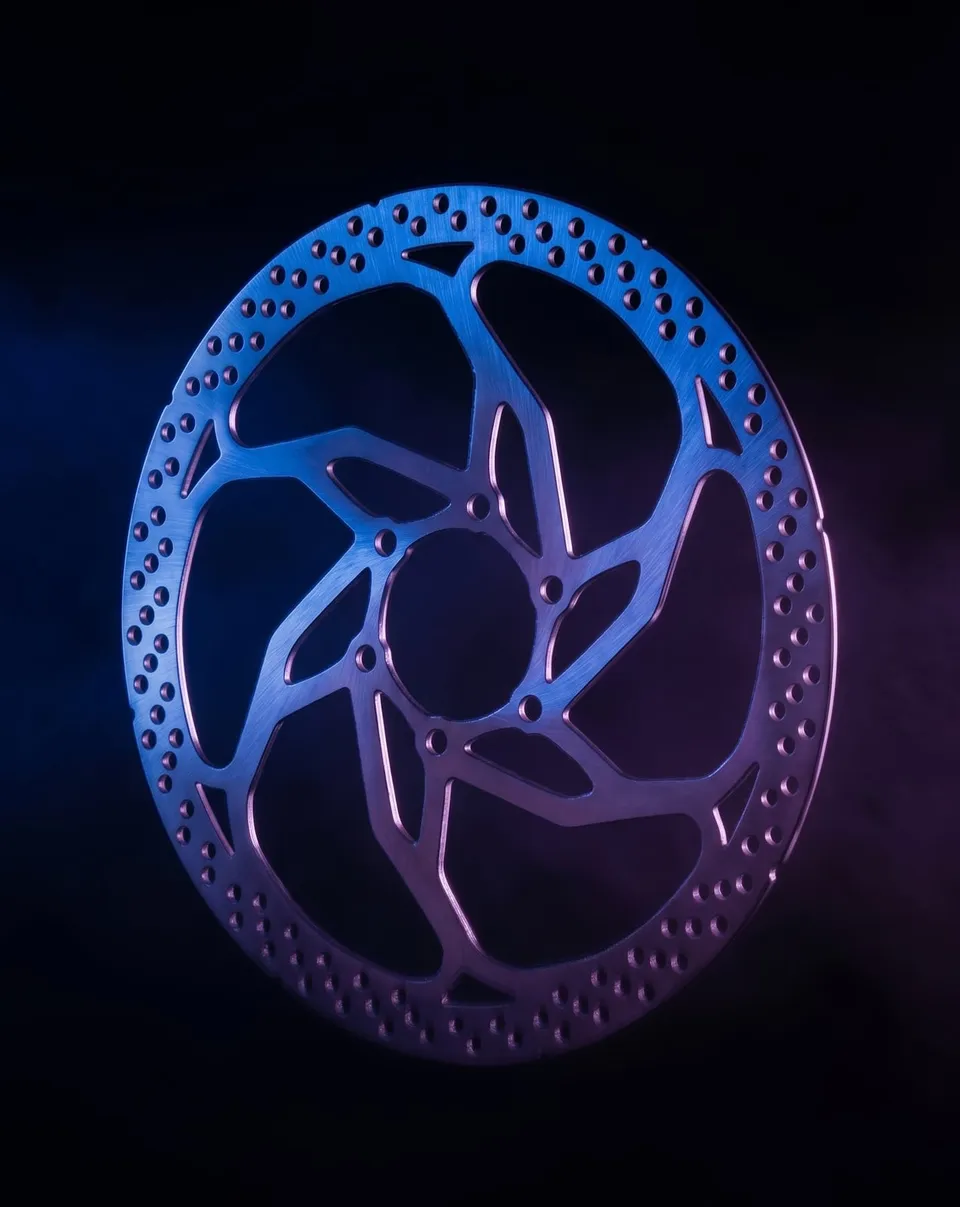 Disc de fre de bicicleta d’acer inoxidable tallat amb làser, il·luminat en blau i violeta sobre negre